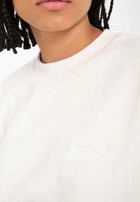 Hvid fleece sweatshirt med ribbet rund hals og struktureret logo-patch. Blødt, letvægtsstof og en afslappet pasform.