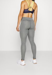 Szare legginsy z wysokim stanem, wykonane z elastycznego materiału, w połączeniu z ciemnoniebieskim biustonoszem sportowym z żółtymi ramiączkami. Całość dopełniają białe sneakersy.