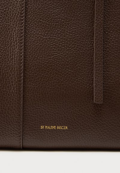 Καφέ δερμάτινη τσάντα με υφή από ψιλά στίγματα, απλό σχέδιο και χρυσό ανάγλυφο όνομα μάρκας "BY MALENE BIRGER" στο μπροστινό μέρος.