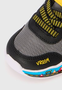 Sapatilha em malha cinza com detalhes em preto, tiras elásticas amarelas e "VROOM" impresso em amarelo. Sola colorida que imita o padrão de uma estrada com detalhes.