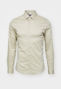Camicia da uomo beige a maniche lunghe, aderente, con colletto a punta e bottoni sul davanti, su uno sfondo bianco.