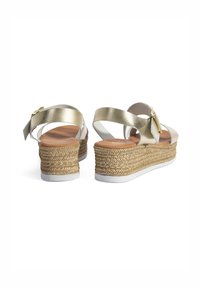 Sandales compensées métalliques dorées avec un talon en jute tressé et une semelle en caoutchouc blanc, dotées d'une sangle croisée et d'une boucle ajustable à la cheville.