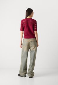Bordeauxfarbendes Strickshirt mit kurzen Ärmeln und Ausschnittdetails, kombiniert mit hellblauen lässigen Jeans. Glatte Textur, lockere Passform.