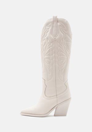 Botte de cowboy en cuir blanc avec bout pointu, talon bloc incliné et motifs floraux cousus sur la tige.
