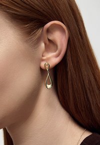 Złote kolczyki w kształcie łezki z polerowanym wykończeniem. Projekt zawiera dekoracyjną pętelkę na górze, podkreślając nowoczesny styl.