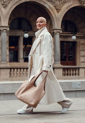 Hellbeige Leder-Tote mit geschwungenen Griffen, getragen mit einem langen weißen Mantel und einem cremefarbenen Rollkragenpullover. Weiße Sneakers; glatte, minimalistische Textur.