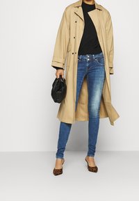 Beige trenchcoat, svart tröja, blå skinny jeans och leopardmönstrade klackar. Trenchcoaten har stora knappar och sidofickor.
