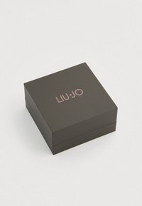 Mustast materjalist ehetekast mattviimistlusega ja roosakuldse "LIU•JO" logoga peal. Omab hingedega kaant ja siledad servad.