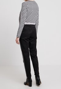 Černé kalhoty s bílými bočními pruhy, s upraveným střihem a hladkou texturou. Vybavené vzorovaným černobílým topem s dlouhým rukávem.