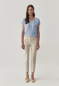 Světle modrý, krátký rukáv s výstřihem do V a švy. Krémové, ušité kalhoty s vertikálními švy a slim fit. Béžové baleríny.