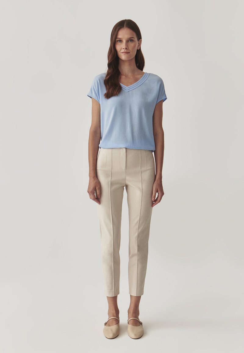 Světle modrý, krátký rukáv s výstřihem do V a švy. Krémové, ušité kalhoty s vertikálními švy a slim fit. Béžové baleríny.