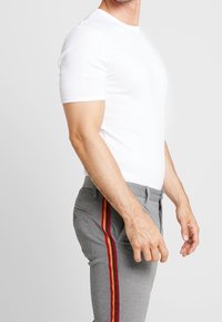 Biała koszula z krótkim rękawem w połączeniu z szarymi spodniami z czerwono-żółtymi bocznymi paskami. Spodnie zapinane na guzik i zamek błyskawiczny.