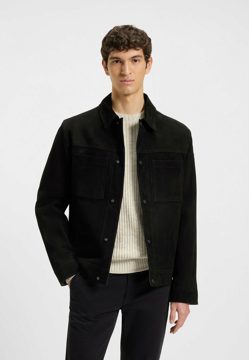 Svart mockajacka med två framfickor, tryckknappar och krage, bärs över en ljusstickad tröja. Slim fit, texturerad yta.