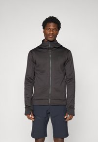 Felpa nera con zip realizzata in tessuto elasticizzato, con colletto alto, caratterizzata da un piccolo logo sul petto e aperture per il pollice nei polsini.