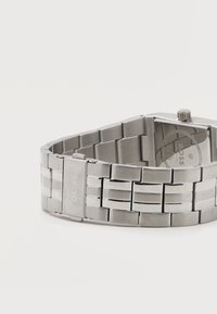 Ασημένια μεταλλική μπάντα ρολογιού με αγκράφα χαραγμένη με τη λέξη "BOSS" και ορατή πίσω πλευρά ρολογιού με σήμανση και κορώνα.