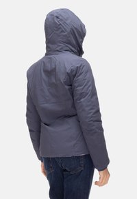 Giacca con cappuccio viola dal design imbottito, con chiusura a cerniera. La parte posteriore presenta una texture liscia e dettagli minimi. Indossata con jeans blu.