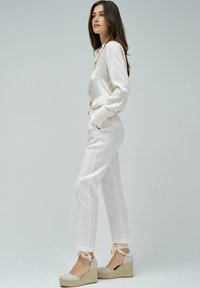 Blouse blanche à rayures, pantalon blanc court, et sandales à semelle compensée beige avec des accents en ruban. Tissu lisse, coupe ajustée et lignes épurées.