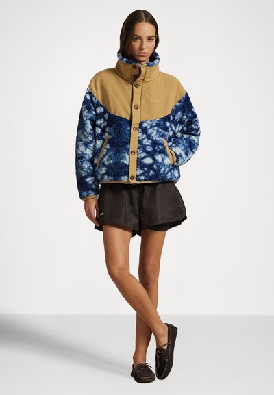 Μπλε και καφέ fleece ζακέτα με ψηλό γιακά, κούμπωμα με κουμπιά και δύο πλαϊνές τσέπες. Διαθέτει υφή με σχέδιο σύννεφων.