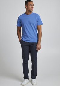 T-shirt di cotone azzurro chiaro con maniche corte e scollo rotondo, abbinato a pantaloni navy scuri e sneakers bianche. Tessuto liscio, vestibilità casual.