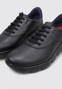 Zapatos de cuero negro con un acabado suave, punta redondeada y suelas de goma planas. Cuentan con un cierre de cordones negro y un interior de color azul marino.