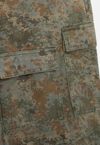 Tarncargo-Hose in grünen, braunen und beigen Tönen, mit zwei vorderen Taschen und einem strukturierten Stoff mit einem verblassten Aussehen.