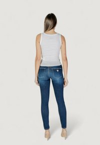 Jeans in denim blu con vestibilità slim, dotati di vita medio-alta, tasche posteriori e una leggera elasticità. Abbinati a un top bianco senza maniche.