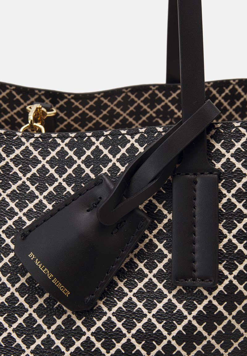 Black and white patterned handbag with textured synthetic material, featuring a leather tag and gold lettering, and black leather accents.