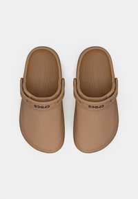 Sabots Crocs marron avec un matériau texturé, une sangle arrière et un détail de logo. La vue de dessus montre des lignes lisses et un design moulé.