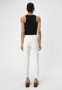Schwarzes, geripptes Tanktop mit weißen, taillierten Hosen mit elastischem Bund und Seitentaschen, kombiniert mit braunen Blockabsatzsandalen.