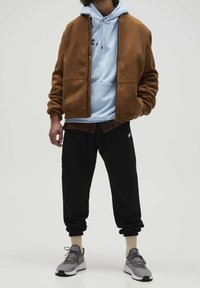 Bruine fleecejack, lichtblauwe hoodie eronder, zwarte joggers en grijze sneakers. Opvallende texturen zijn fleece en katoen.