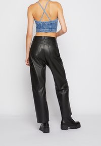 Top corto de mezclilla con tirantes entrecruzados, pantalones de cuero negro de pierna ancha y botas de plataforma negras. Textura suave con bolsillos funcionales.