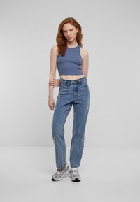 Svetlo modra skrajšana majica brez rokavov v kombinaciji z modrimi hlačami z visokim pasom in sivi športni čevlji. Tekstura je gladka in se prilega sproščenemu slogu.