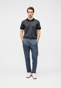 Μαύρο πόλο πουκάμισο με υφασμένο σχέδιο, συνδυασμένο με ανοιχτό μπλε ριγέ παντελόνια και λευκά αθλητικά παπούτσια με καφέ λεπτομέρειες.