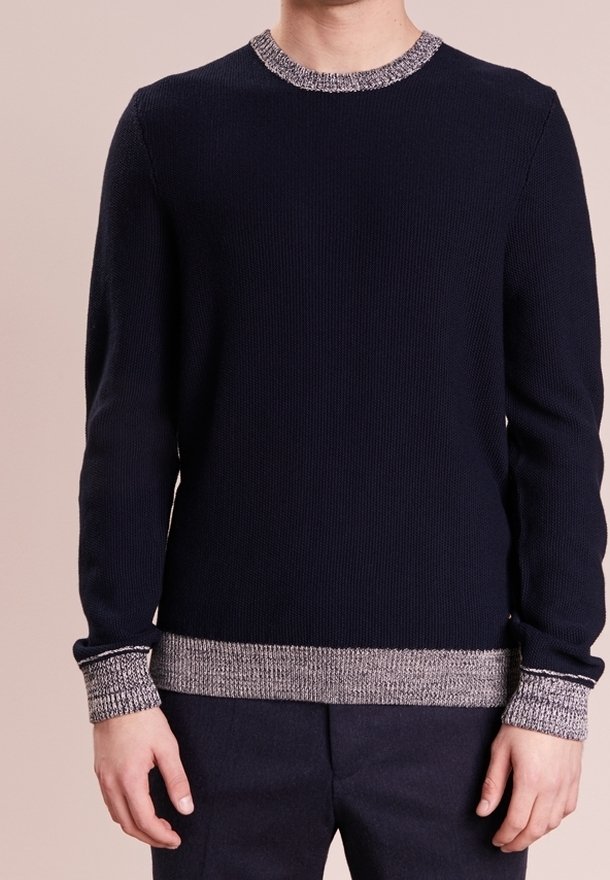 Homme portant un pull bleu marine foncé avec des poignets, un col et un ourlet côtelés gris clair, associé à un pantalon sombre.