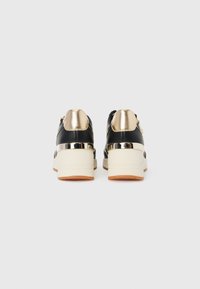 Black sneakers with gold accents and a white platform sole. Features a metallic heel and zipper detail on the back. Smooth texture.