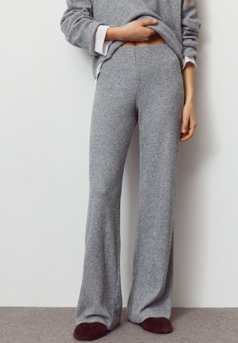 Sive pletene hlače širokih nogavica s rebrastom teksturom, s elastičnim pojasom i ležernim krojem. Nošene s labavim sivim džemperom.