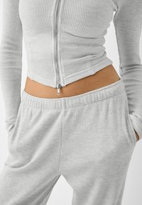 Grå ribbad zip-up topp med långa ärmar, tillsammans med matchande grå byxor med elastisk midja. Tyget har ett strukturerat mönster.