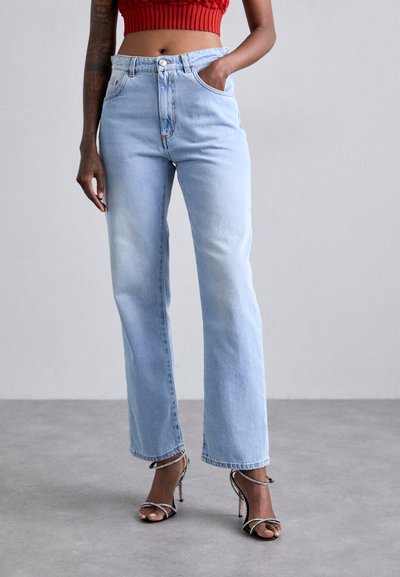 Jeans de mezclilla anchos de color azul claro con cintura alta, que cuentan con dos bolsillos frontales y un ligero desgaste. Combinados con tacones negros con tiras.