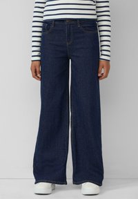 Wijduitlopende donkerblauwe denim jeans met een hoge taille en een traditionele vijf-pocket ontwerp, gecombineerd met witte sneakers.