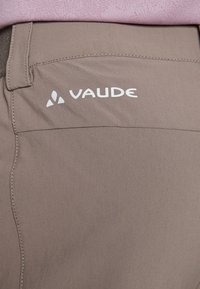 Bruine Vaude-broek met een gladde textuur en zichtbare stiksels, met een wit logo op de zijkant. Eenvoudig, functioneel ontwerp.
