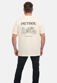 Crèmefarvet bomulds T-shirt med et grafisk design af en motorcykel på ryggen, med ordet "PETROL" i fede bogstaver ovenfor.