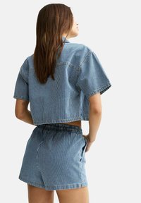 Conjunto de denim a rayas azules y blancas que incluye una camisa corta de manga corta y pantalones cortos con cintura elástica, con un diseño casual.