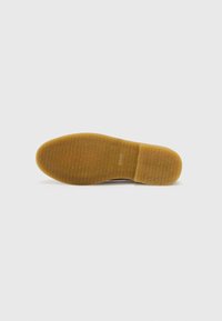 Semelle de chaussure en caoutchouc avec une surface texturée et à motif marron. Présente un bord lisse et le nom de la marque embossé sur le talon.