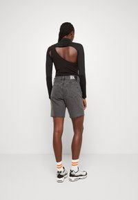 Černé tričko s dlouhým rukávem a výřezem na zádech, spárované se šedými denimovými šortkami s trhanými okraji a logem CK na pásku.