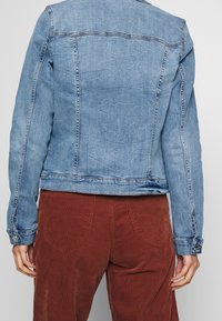 Džínová bunda světle modré barvy s mírně texturovaným povrchem, se strukturovanými švy, dlouhými rukávy a manžetami na knoflíky.