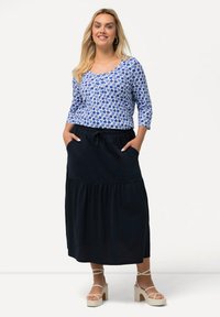 Top blu e bianco con motivo floreale, maniche a tre quarti, abbinato a una gonna lunga nera a livelli con tasche e cintura elastica.
