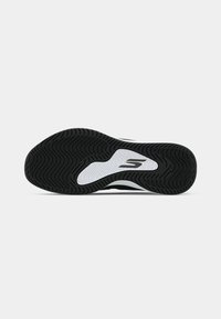 Semelle de chaussure de sport noir et blanc présentant une texture en vagues et des rainures dessinées pour l'adhérence, avec un accent logo central en blanc.