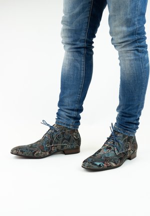 Geplaatste enkellaarsjes van donker stof met blauwe en rode bloemenontwerpen, aangevuld met blauwe veters en een lage hak. Draag je met blauwe jeans.