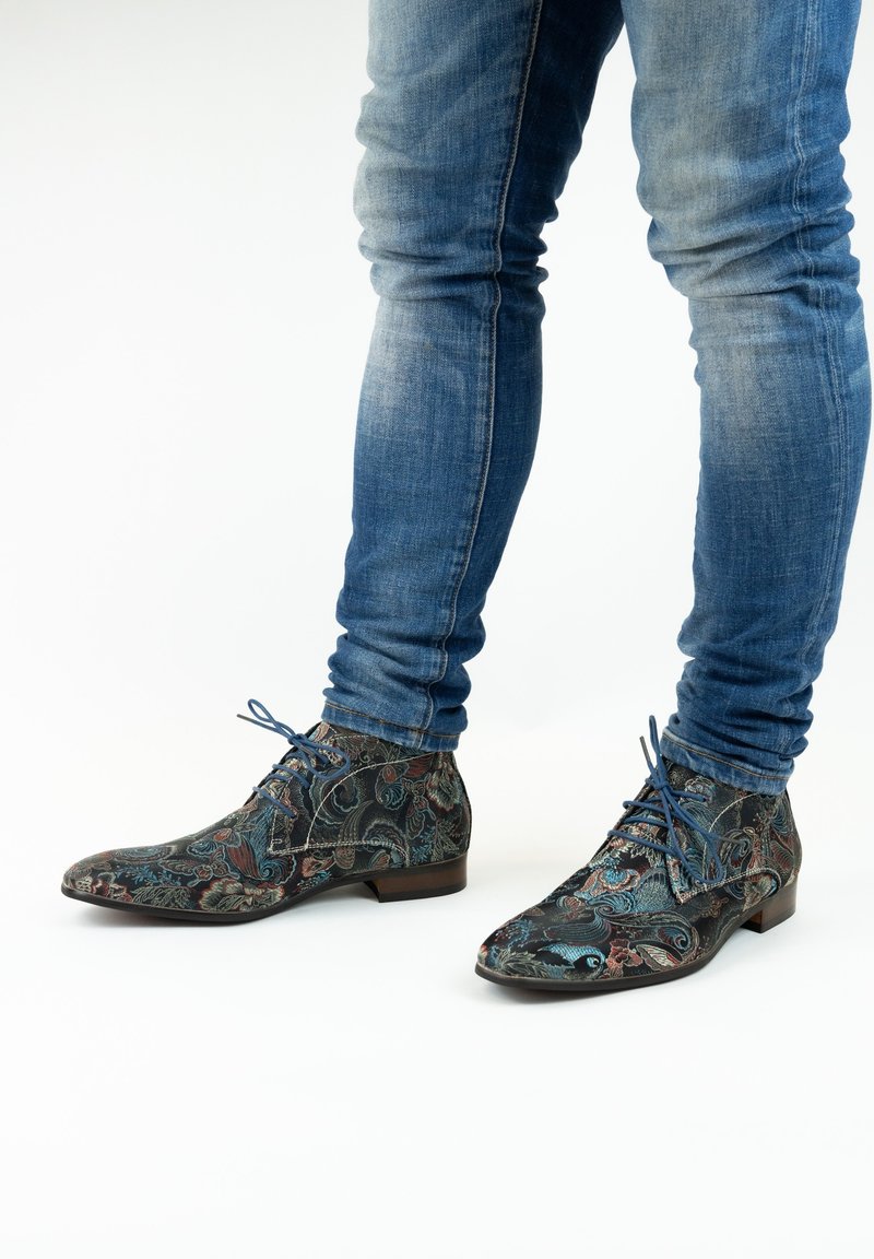 Geplaatste enkellaarsjes van donker stof met blauwe en rode bloemenontwerpen, aangevuld met blauwe veters en een lage hak. Draag je met blauwe jeans.