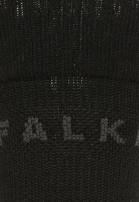Calcetín de punto negro con el nombre de la marca "FALKE" en gris oscuro en la parte superior; textura suave y forma uniforme.